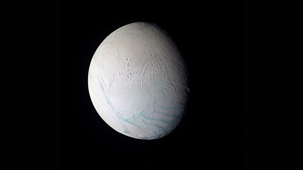 Enceladus in a gibbous phase showing a pristine snow white surface with blue "tiger stripes" near its south pole.